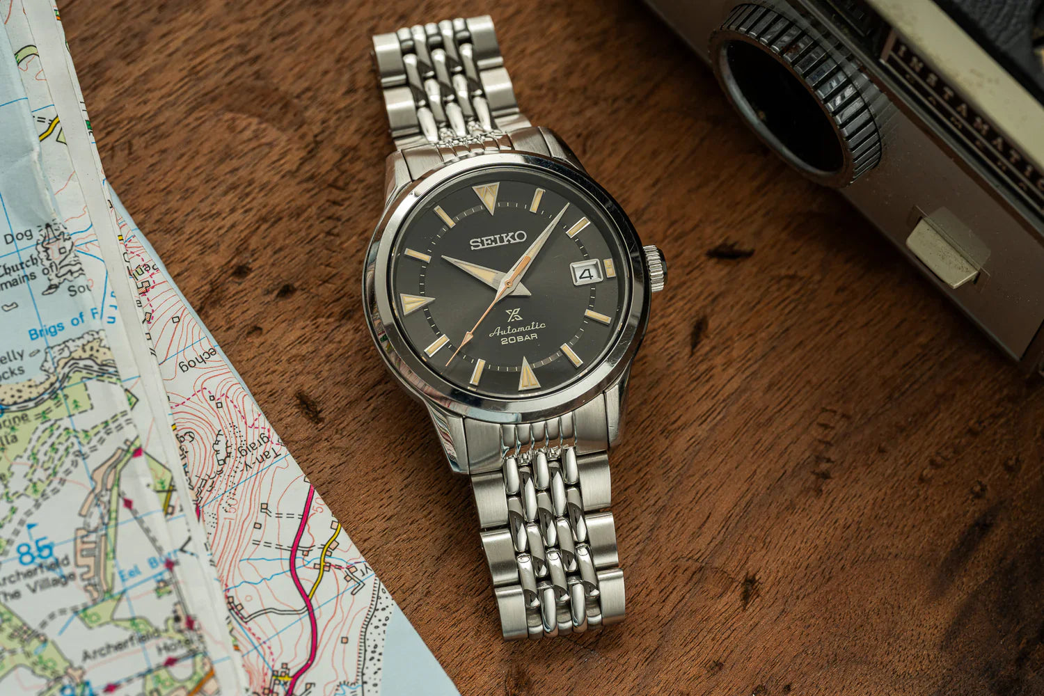 Seiko Alpinist on a beads-of-rice bracelet beside a map and camera